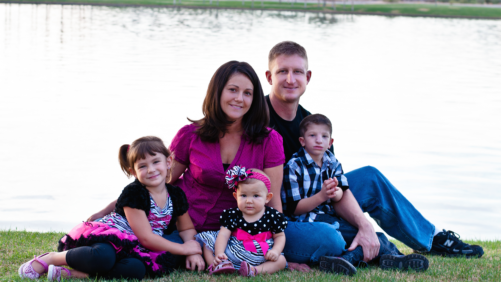 Mom Dad two daughters and a son on the grass beside a lake