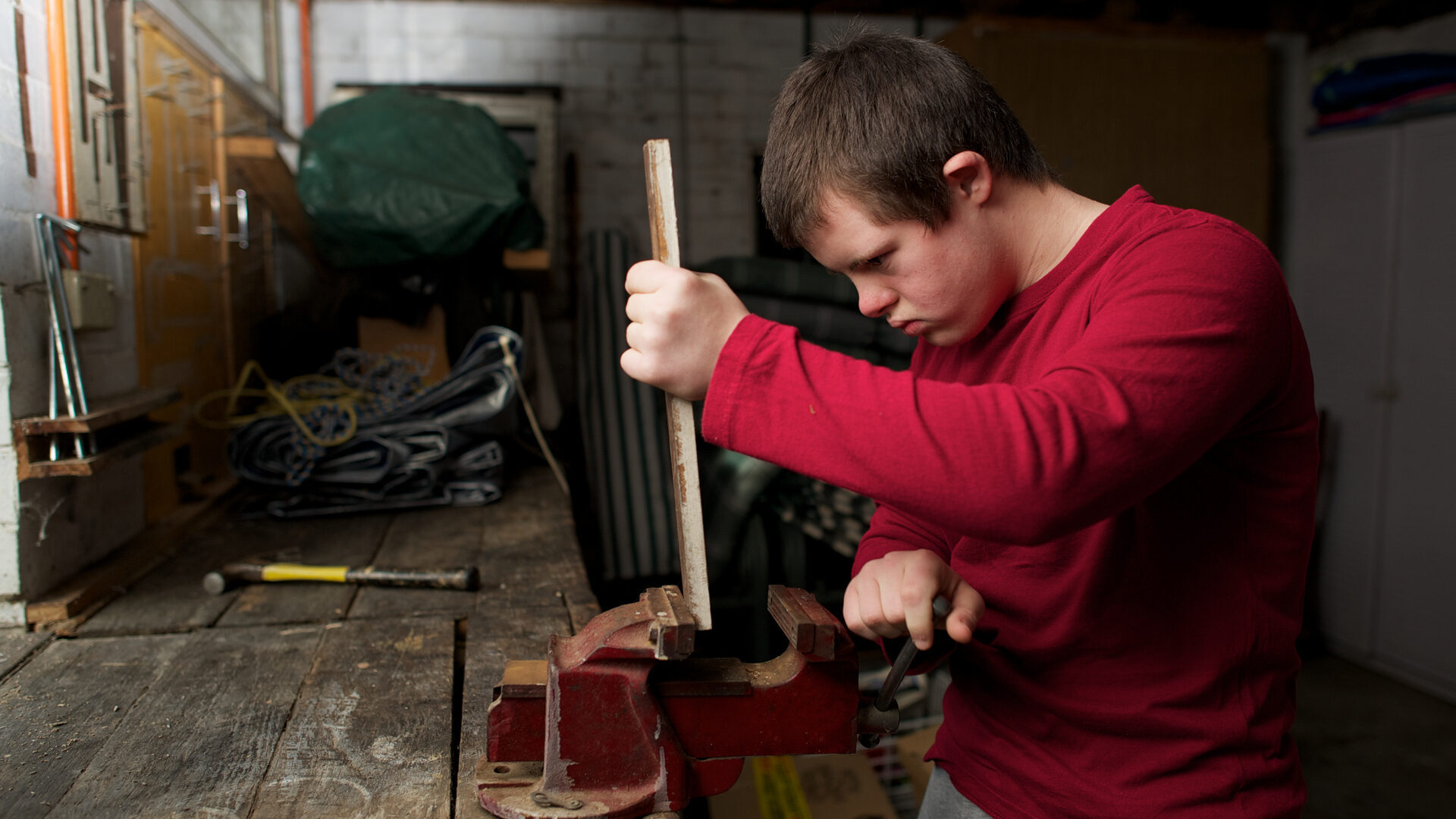 Teenager with Down syndrome placing wood in a vice in a workshop