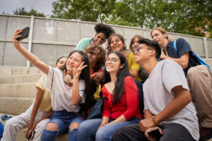 Group of multiracial students taking selfies with mobile phone. Asian girl shows her fingers