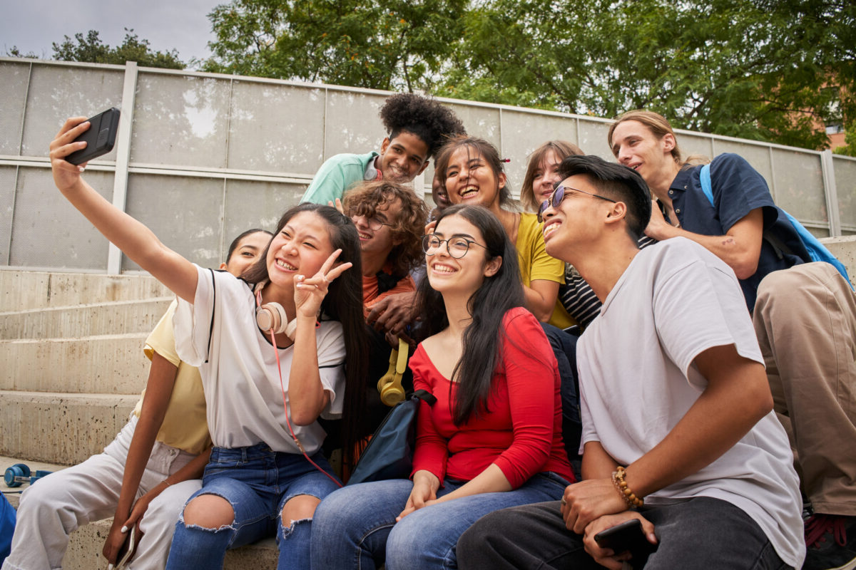 Group of multiracial students taking selfies with mobile phone. Asian girl shows her fingers